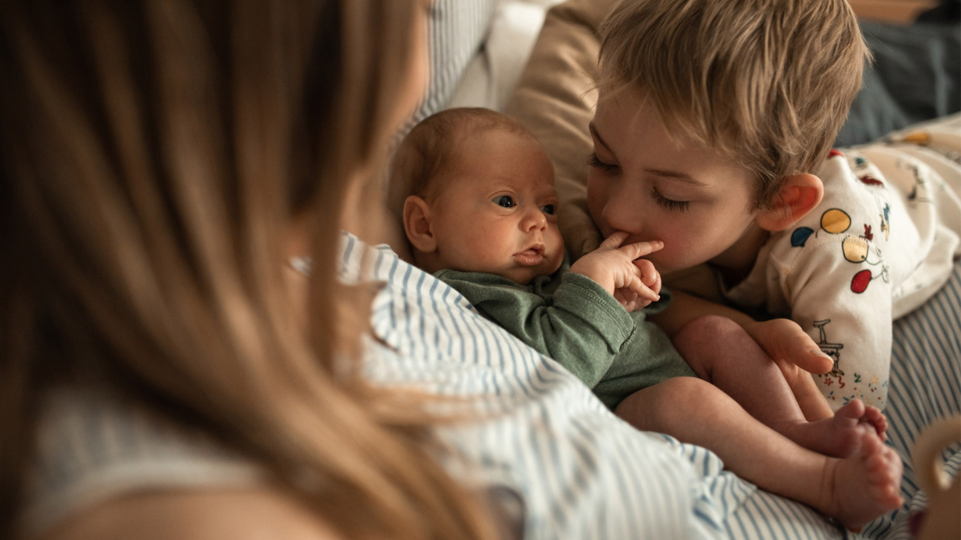 A newborn baby is held by his mother and kissed by his older brother.